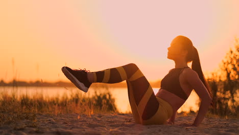 Junge-Schöne-Sportlerin,-Die-Am-Strand-Bei-Sonnenuntergang-Übungen-Für-Die-Bauchmuskulatur-Macht-Und-Sich-In-Zeitlupe-Dreht